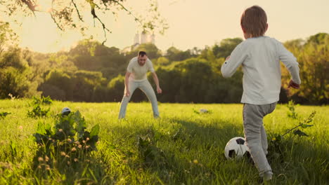 Young-father-with-his-little-son-playing-football-on-football-pitch